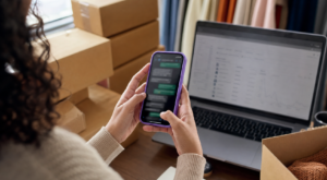 lojista usando WhatsApp marketing em um celular sobre bancada de ecommerce com detalhe roxo na cena